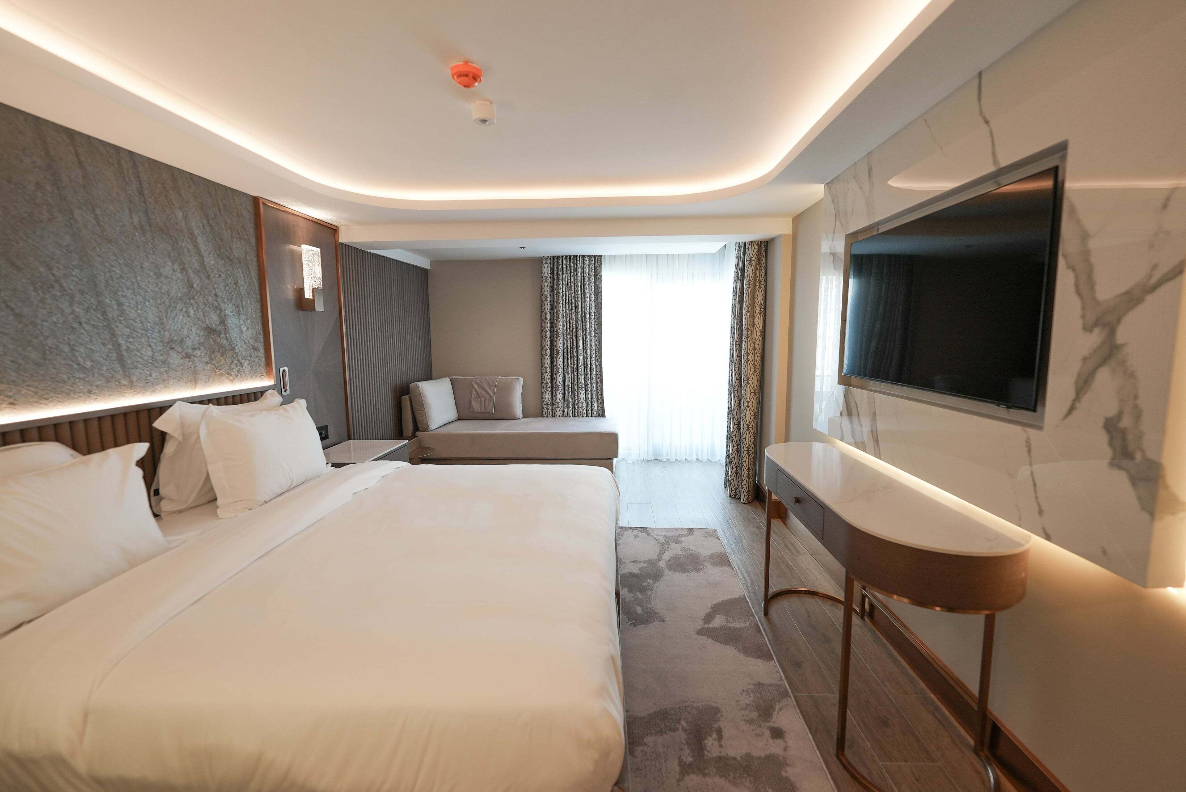 Una habitación de hotel moderna con una cama grande, una zona de estar, un televisor y una pared de mármol.