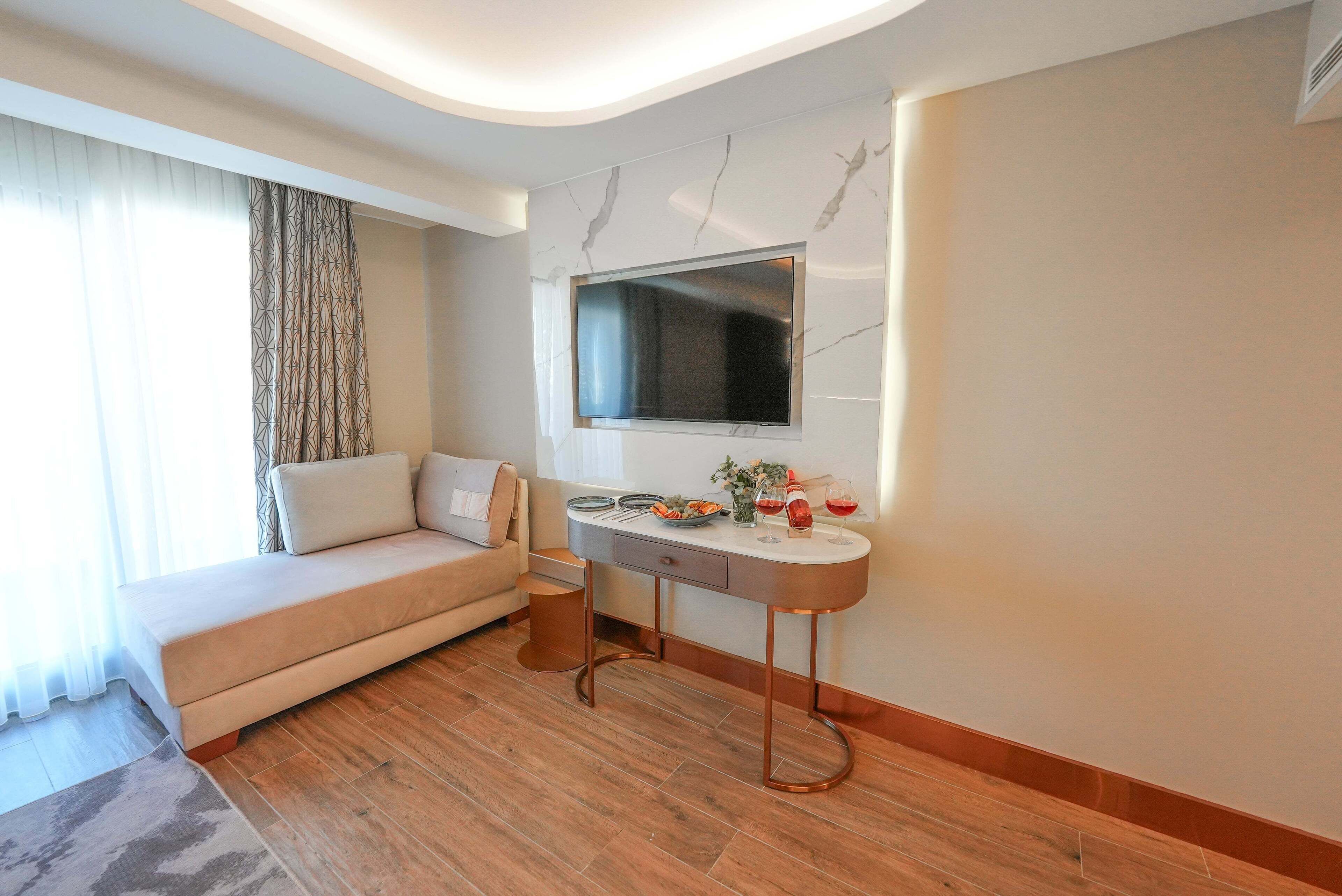 A modern hotel room with a sofa, a dining table, and a flat-screen TV mounted on the wall.