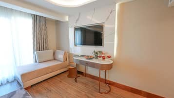 A modern hotel room with a sofa, a dining table, and a flat-screen TV mounted on the wall.