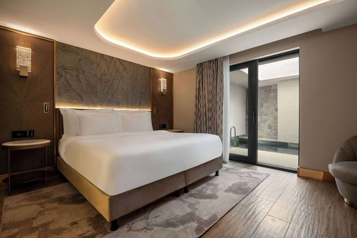 Ein modernes Hotelzimmer mit einem großen Bett, einem Nachttisch, Wandkunst, einer Duschkabine und einer Sitzecke.