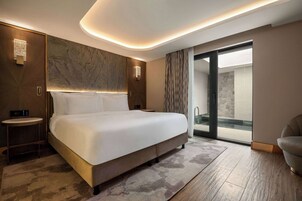 Una habitación de hotel moderna con una cama grande, una mesita de noche, un cuadro integrado en la pared, una zona de ducha y un área de descanso.