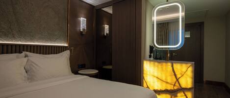 A modern hotel room with a large bed, a vanity with a mirror, and a unique wall design.