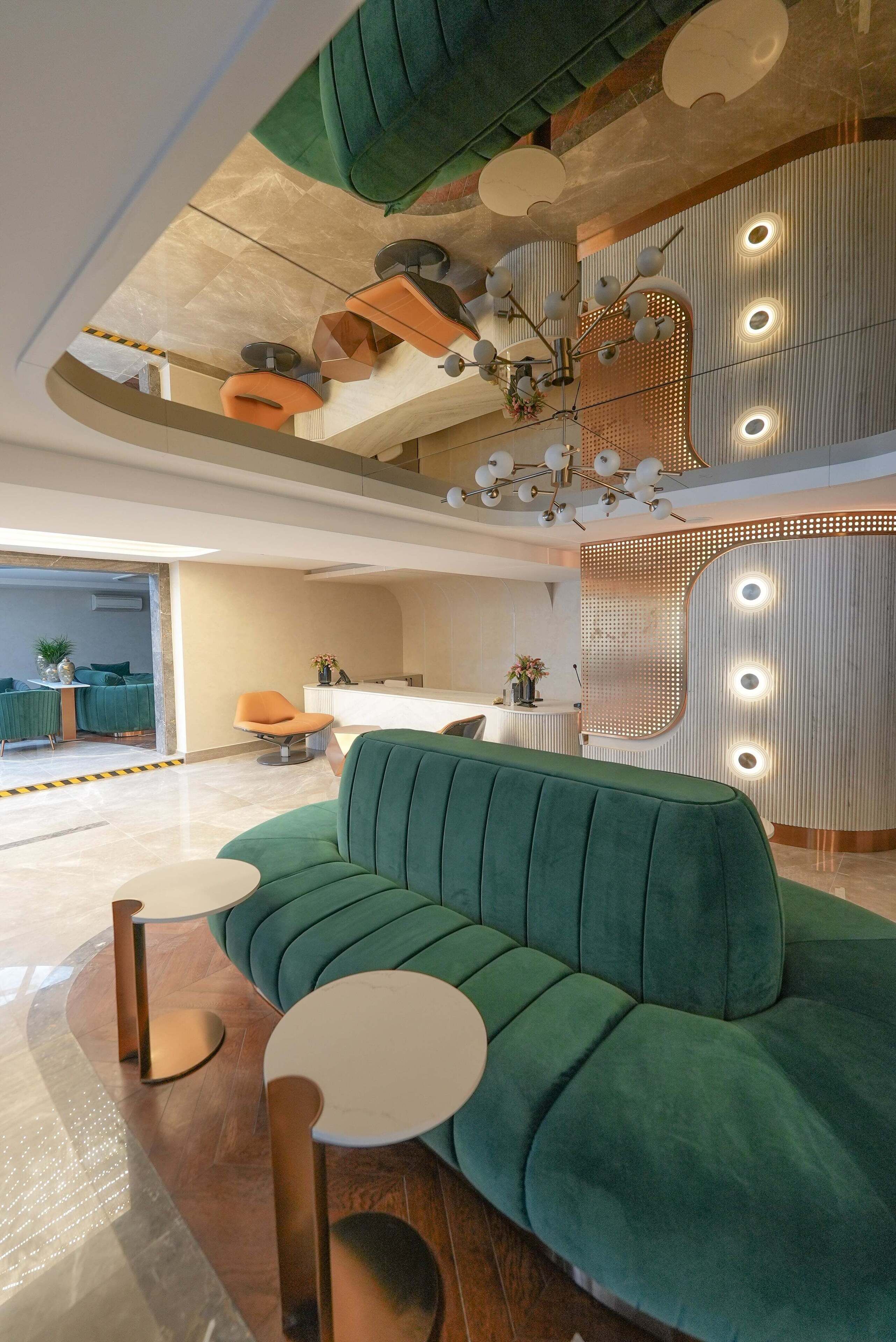 Un hall moderno con un sofá verde, mesas redondas y un mostrador de recepción.