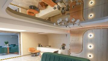 Un hall moderno con un sofá verde, mesas redondas y un mostrador de recepción.