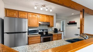 A modern kitchen with wooden cabinets, stainless steel appliances, granite countertops, and a built-in oven.