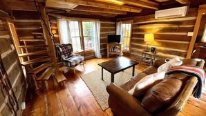 A log cabin interior with a wooden floor, a sofa, a chair, a coffee table, a TV, and a lamp.