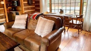 A cozy cabin interior with a leather sofa, wooden walls, a dining table, and a kitchen area.