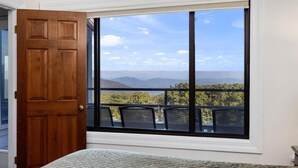 Una habitación con un ventanal amplio que ofrece vistas a la montaña, una puerta de madera y una cama con colcha estampada.
