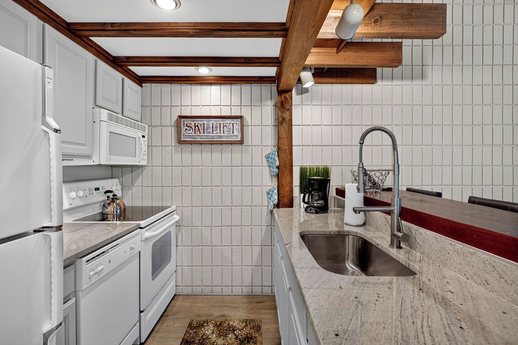 Una cocina con armarios blancos, un lavamanos de acero inoxidable y una viga de techo de madera.