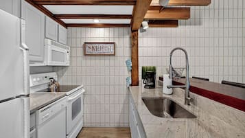 Una cocina con armarios blancos, un lavamanos de acero inoxidable y una viga de techo de madera.