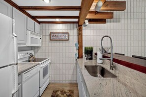 Une cuisine avec des meubles blancs, un évier en acier inoxydable et une poutre en bois au plafond.