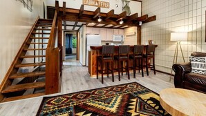 L’intérieur d’une cabane comprend un escalier en bois, un coin cuisine et un espace salon agrémenté d’un tapis à motifs.