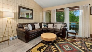 Un salon avec un canapé d’angle en cuir marron, une table basse ronde en bois, un grand miroir et un tapis à motifs.