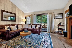 Un salon avec un canapé en cuir marron, un tapis à motifs, une table basse en bois et une grande fenêtre avec des rideaux.