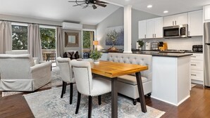 Une cuisine moderne avec des meubles blancs, un îlot central et un coin repas comprenant une table en bois et des chaises à revêtement blanc.