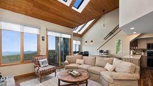 A spacious living room with a large sectional sofa, a wooden coffee table, and a view through large windows.