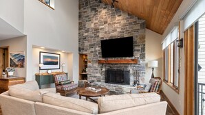 A cozy living room with a stone fireplace, comfortable seating, and a large TV mounted on the wall.