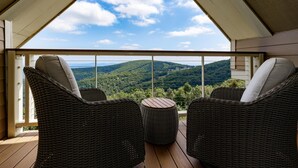 Un balcón con sillas de mimbre y una pequeña mesa redonda, con vistas a un paisaje pintoresco con colinas y árboles.