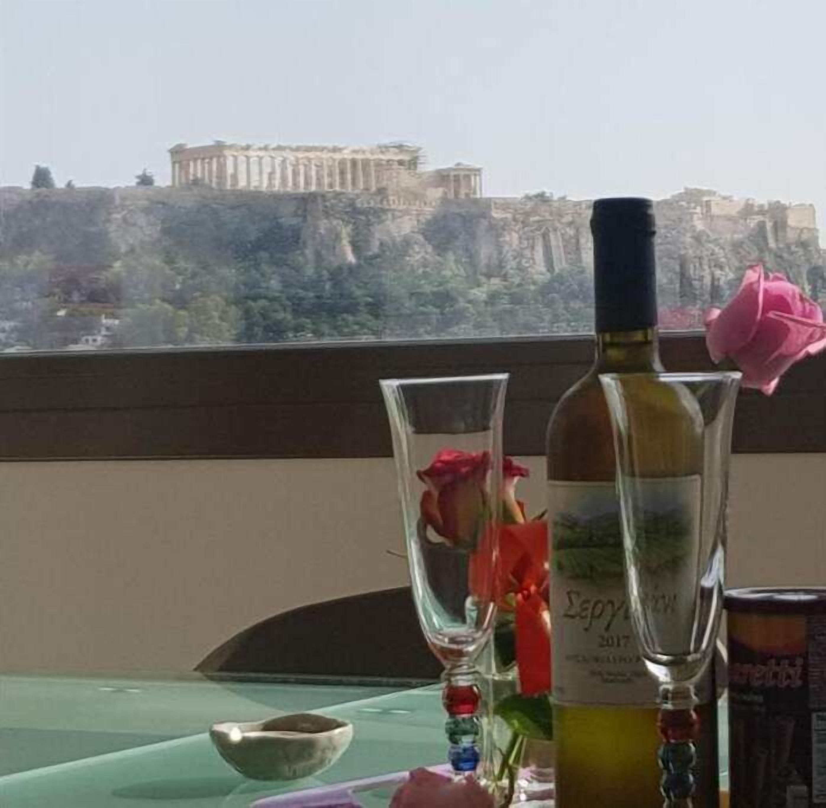 A table with a bottle of wine, a glass, and a bowl. A rose is placed on the table. In the background, there is a view of a historical building.