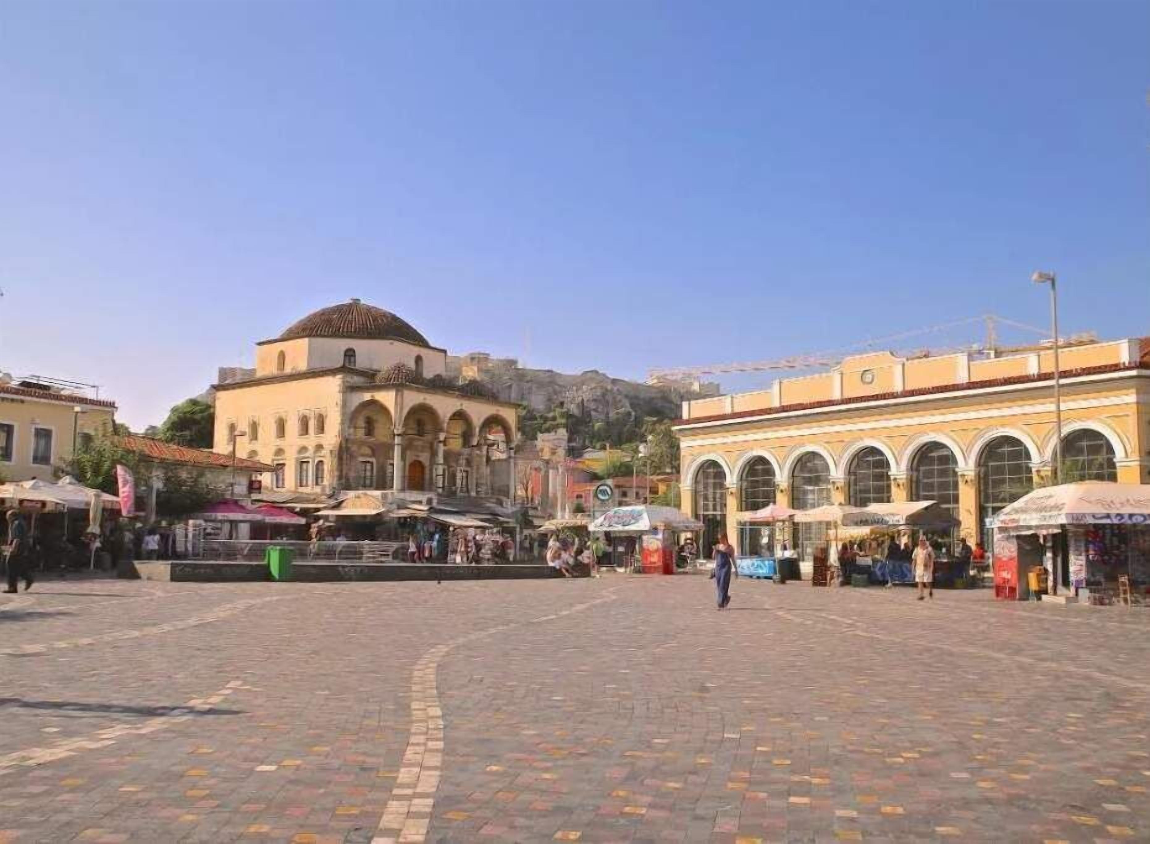 A public square with a historic building featuring arches and a dome, surrounded by shops and cafes.