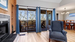 A living room with a fireplace, a sliding glass door leading to a deck, and a dining area with wooden furniture. - Stoneridge 69 with Wintergreen Advantage (Wintergreen)