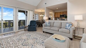 A spacious living room with a large sliding glass door leading to a balcony, a cozy seating area with a sofa and armchairs, and a kitchen in the background. - Northridge 09 with Wintergreen Advantage (Wintergreen)