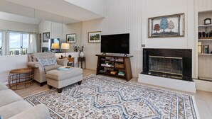 A living room with a sofa, ottoman, and a fireplace. There is a television on a stand and a large rug on the floor. - Northridge 09 with Wintergreen Advantage (Wintergreen)
