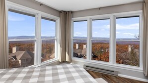 Quarto com grandes janelas, edredom xadrez e vista para uma paisagem montanhosa.