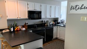 A modern kitchen with white cabinets, a black microwave, and a coffee maker. There are wooden stools and a stainless steel trash can. - Shenandoah Ridge 07 with Wintergreen Advantage (Wintergreen)