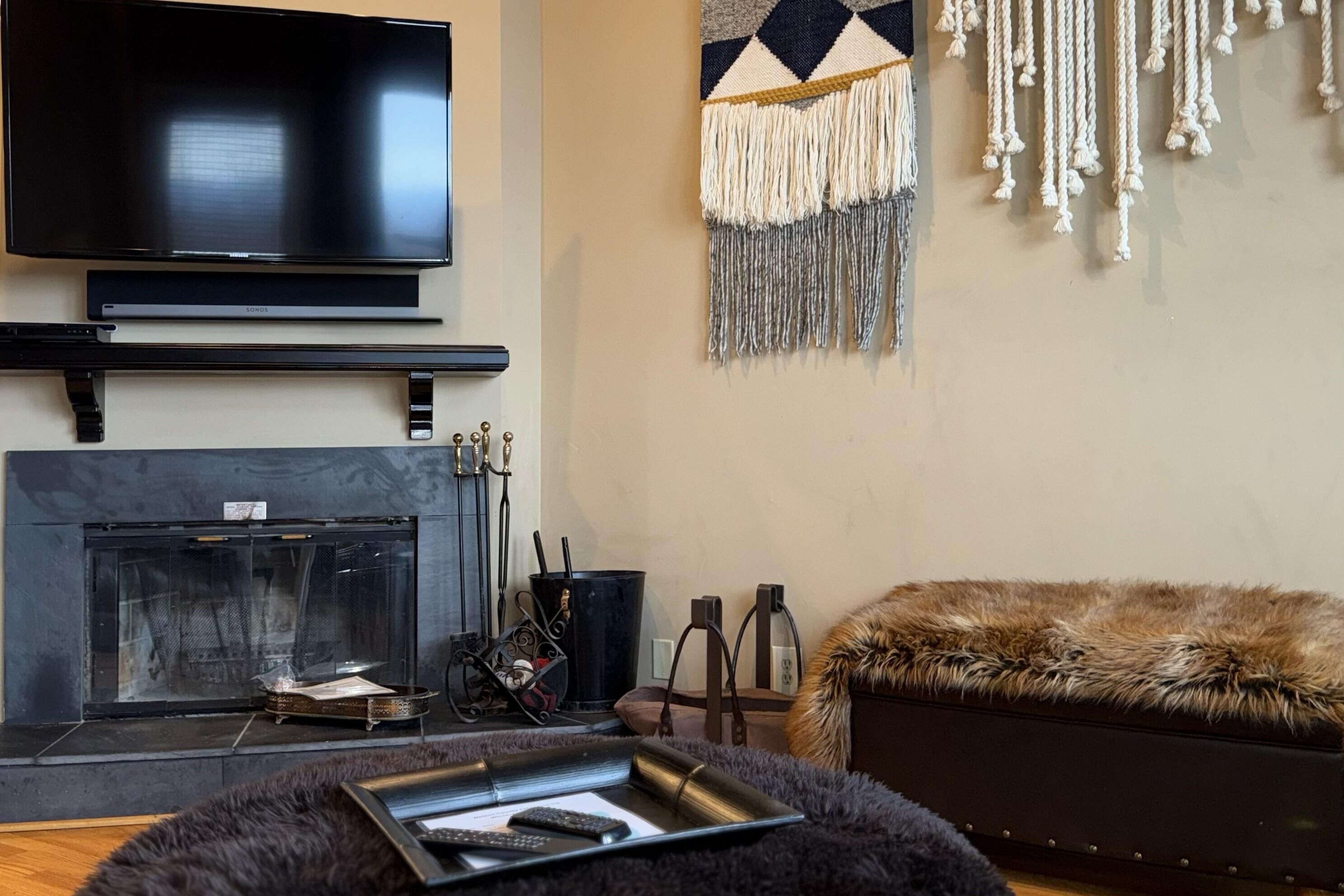 A modern living room with a flat-screen TV, fireplace, and a cozy fur-covered ottoman.