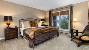 A bedroom with a large bed, two bedside tables with lamps, a chair, and a window with curtains.