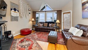 A living room with a brown leather sofa, a red ottoman, a patterned rug, and a fireplace with a decorative mantle.