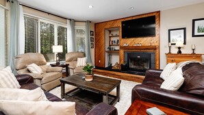 Ein Wohnzimmer mit Kamin, Ledersofas, einem Couchtisch und einem an der Wand befestigten Fernseher.