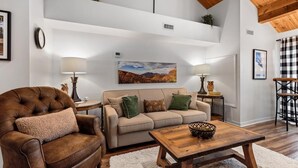 A living room with a brown leather armchair, a beige sofa, and a wooden coffee table. There is a painting on the wall, a clock, and a plant on a shelf. - Mountain Inn Lodge 55 with Wintergreen Advantage (Wintergreen)