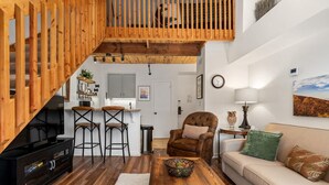 A spacious living area with a wooden staircase, a sofa, a coffee table, and a TV stand. - Mountain Inn Lodge 55 with Wintergreen Advantage (Wintergreen)