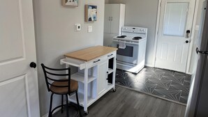 Una cocina compacta con estufa blanca, una mesa de madera y una silla.