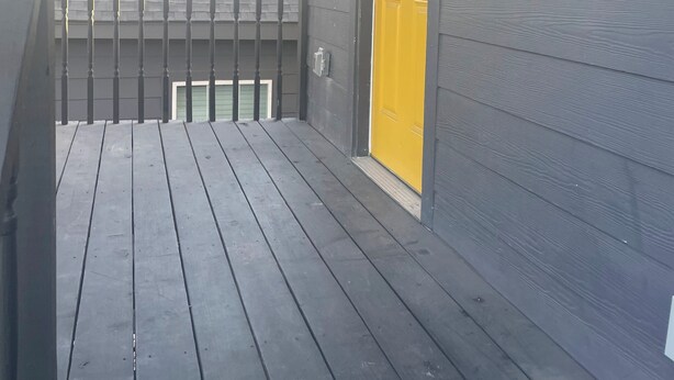 Una terraza de madera con una puerta amarilla y una lámpara.
