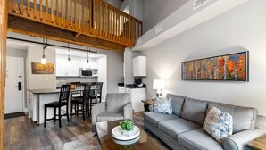 Un salon moderne avec un canapé gris, une table basse et un coin repas comprenant des chaises, et une cuisine en arrière-plan.