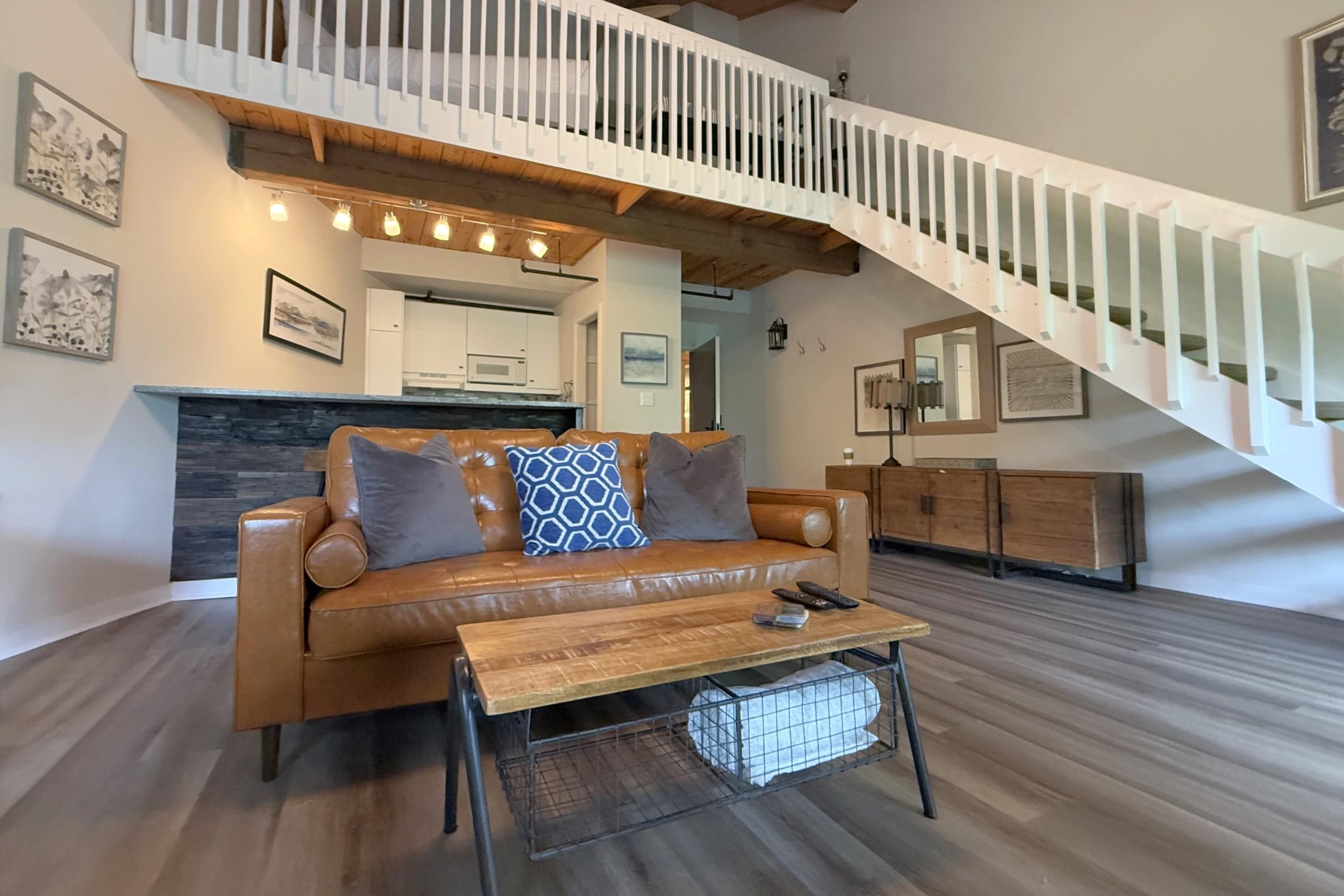 A modern living room with a leather sofa, a wooden coffee table, and a staircase with white railings.