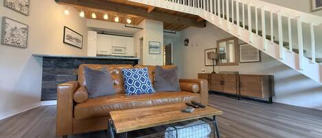 A modern living room with a leather sofa, a wooden coffee table, and a staircase with white railings.