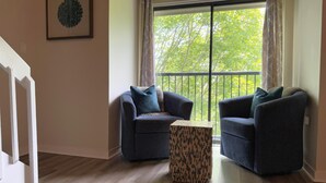 A living room with two dark blue armchairs, a patterned ottoman, a large window with curtains, and a framed artwork on the wall. - Mountain Inn Lodge 62 with Wintergreen Advantage (Wintergreen)