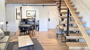 Un espacio habitable moderno estilo loft, con escalera de madera, comedor con mesa y sillas, y área de cocina con estufa y armarios.