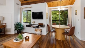A modern living room with a wooden ceiling, a round dining table with four chairs, a TV mounted on the wall, and large windows with a view of greenery. - Mountain Inn Lodge 64 with Wintergreen Advantage (Wintergreen)