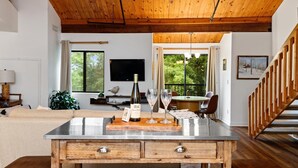 A modern living room with a wooden ceiling, a dining area with a table and chairs, a TV mounted on the wall, and a staircase with wooden railings. - Mountain Inn Lodge 64 with Wintergreen Advantage (Wintergreen)