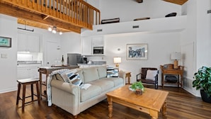 A spacious living area with a wooden coffee table, a sofa, and a dining table. A kitchen with white cabinets and a microwave is visible in the background. - Mountain Inn Lodge 64 with Wintergreen Advantage (Wintergreen)