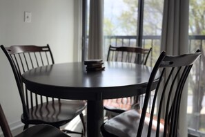 A round dining table with four chairs, a stack of books on the table, and a view of trees through large windows.