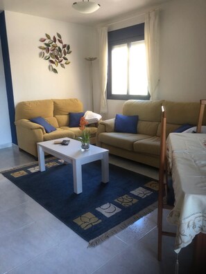 Ein Wohnzimmer mit zwei Sofas, einem Couchtisch, einer Lampe und einem Fenster mit Vorhängen.