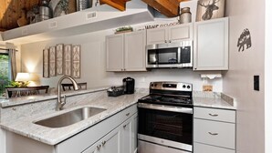 A modern kitchen with white cabinets, stainless steel appliances, a granite countertop, and a wooden ceiling.