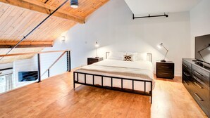 A bedroom with a sloped ceiling, wooden flooring, a bed with a metal frame, bedside tables, a dresser, and a television. - Mountain Inn Lodge 70 with Wintergreen Advantage (Wintergreen)