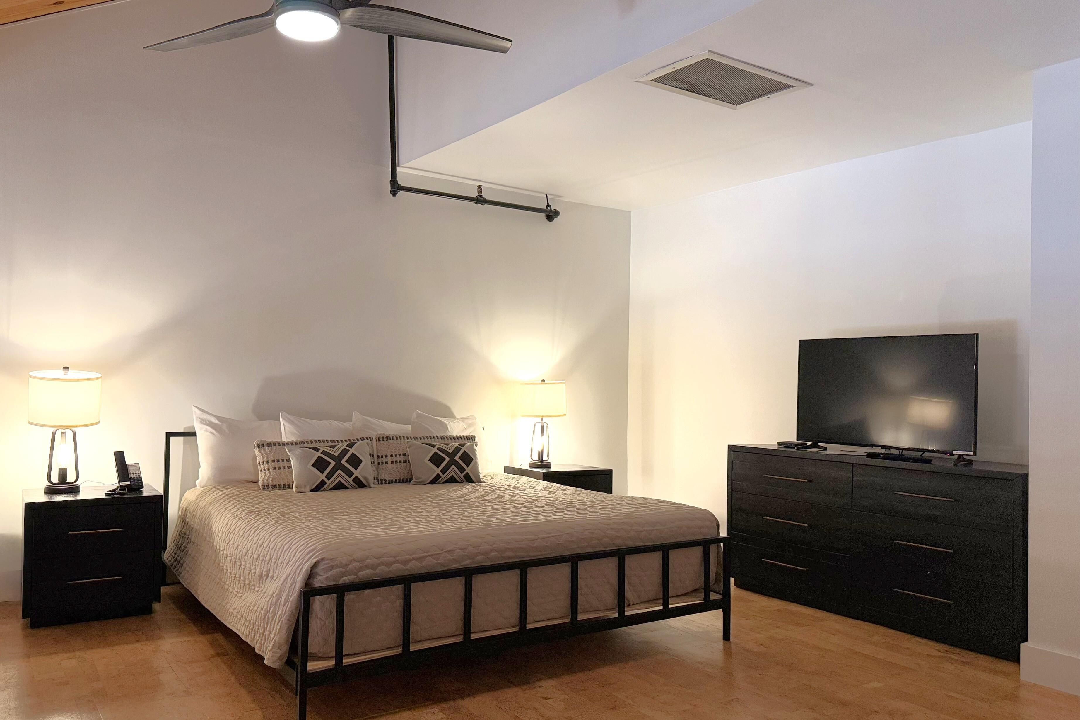Une chambre à coucher avec un lit, des tables de chevet, un téléviseur et un ventilateur de plafond.